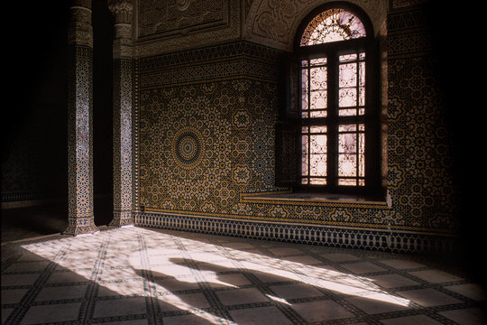 Horizontal image with partial view of a magnificent interior, a facade decorated with stucco and tile mosaics. A window with ornaments and two shadows that appear at the entrance to the room. Kasbah o