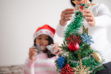 Asian little girl with mother decorating christmas tree for party with happiness,