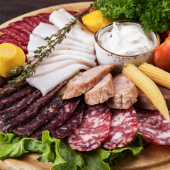 Closeup photo of different sausages with pickled vegetables on wooden board.  Tasty cold appetizer on wooden board. Closeup