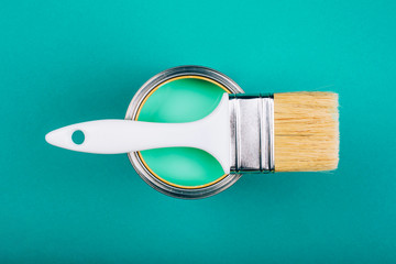 Brush with white handle on open can with turquoise color of paint on blue background. Renovation...