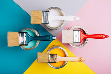 Four open cans of paint with brushes on them on bright symmetry background. Yellow, white, pink,...