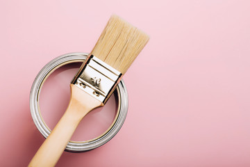 Brush with wooden handle on open can of pink paint on pastel background. Renovation concept. Macro.