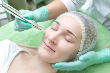 Cosmetologist doing microneedle to a young girl in the beauty salon close up