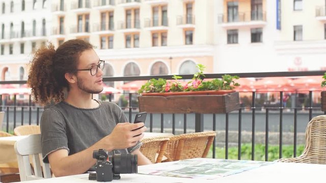 Young guy traveler planning trip for vacation with smartphone and map while sitting at cafe. Slow motion