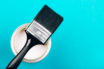 Brush with black handle on open can of white paint on blue background. Renovation concept. Vertical photo.