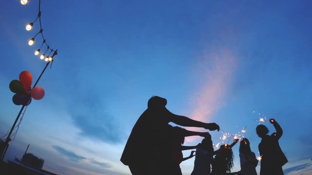 Silhouette of people celebration with friends party holding fireworks together at rooftop with dramatic sky. Concept of festival, happy new year and christmas. 4k resolution.