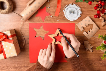 Girl cuts red paper star decoration for Christmas tree on the table surrounded with all kinds of crafting materials