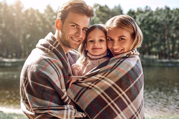 Young parents hugg their little daughter in autumn forest near the lake.