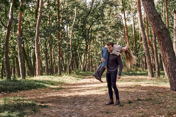 Young man holding his girlfriend on hands in autumn forest.