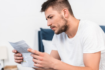 handsome serious man reading newspaper in bed in morning at home