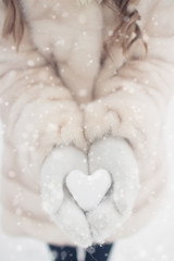 Woman hands are holding a beautiful glossy heart in a snow winter background. Love and St. Valentine cozy concept.