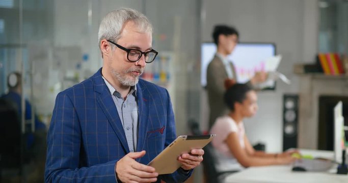 Senior developer using tablet computer for software monitoring in office of information technology company.