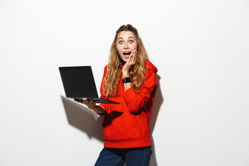 Image of adorable woman 20s wearing red sweatshirt holding laptop, isolated over white background