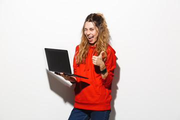 Image of optimistic woman 20s wearing red sweatshirt holding laptop, isolated over white background