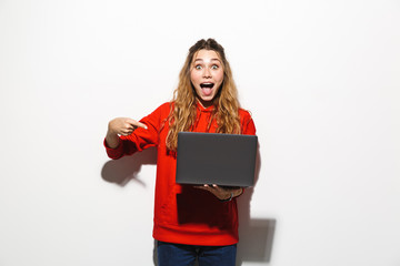 Image of excited woman 20s wearing red sweatshirt holding laptop, isolated over white background