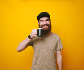 Happy and cheerful bearded hipster man drinking tea or coffee over yellow background