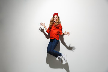 Full length photo of brunette woman 20s wearing red clothes laughing while jumping, isolated over white background