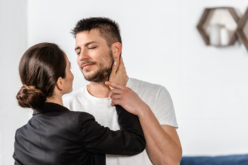 girlfriend in suit going to kiss boyfriend in pajamas in bedroom in morning at weekday, gender...