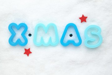 Christmas concept with blue letters, red stars and white snowy background. Festive background with x-mas decoration. Top- view perspective and copyspace.