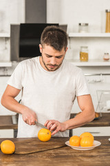 Fototapeta na wymiar handsome man cutting oranges in morning at kitchen