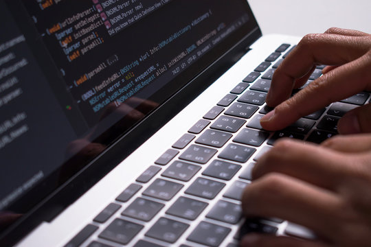 Close up. The developer's hand is creating code on a computer monitor on a white desk.
