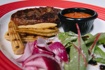 fried meat with garnish of corn with ajika sauce served on a white plate and isolated on a white background. corn steak grill sauce