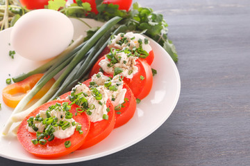 Sliced tomatoes with cheese and herbs on a white plate with onions, sweet peppers and eggs. Close-up. Copy space
