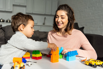 smiling mother and little son playing with colorful plastic blocks at home