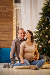 Obraz premium Photo of cheerful pregnant couple on background of decorated New Year tree,Cristmas interior