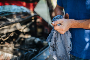 Man wipes his hands with a cloth in front of car - obrazy, fototapety, plakaty