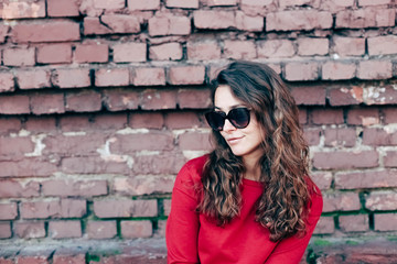 Fototapeta na wymiar Fashionable young girl with long hair, red sweater in sunglasses. Model on brick wall background.