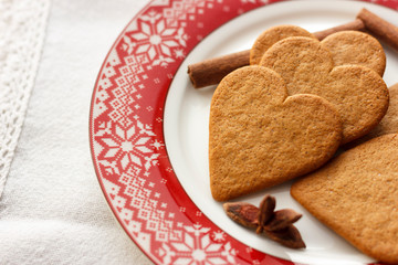 Gingerbread heart-shaped cookies with cinnamon sticks and anise stars on a red plate
