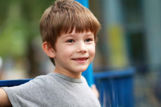 Candid portrait of a happy boy in grey t shirt smiling and sitting on the bench outdoor in the park whose front top milk teeth have fallen out. Close up facial expression, blurred background