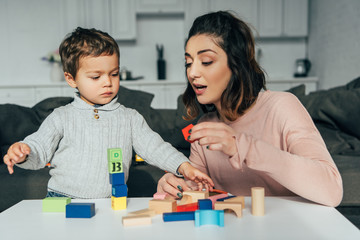adorable little kid and his mother playing blocks wood tower game at home