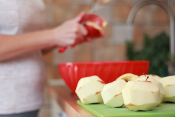 Girl hands is peeling skin off of red apples using a knife