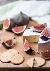 Ripe fresh figs fruits, cheese, cracker on a wooden board with textile towel.