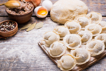 The products for cooking dumplings - flour, dough, minced meat, eggs, spices, bay leaf on a wooden...