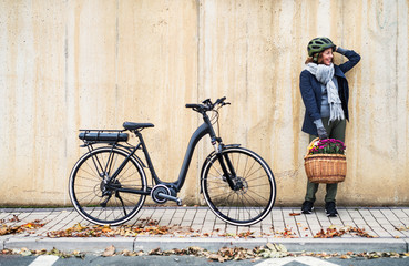 Active senior woman with electrobike standing outdoors in town, leaning against bike.