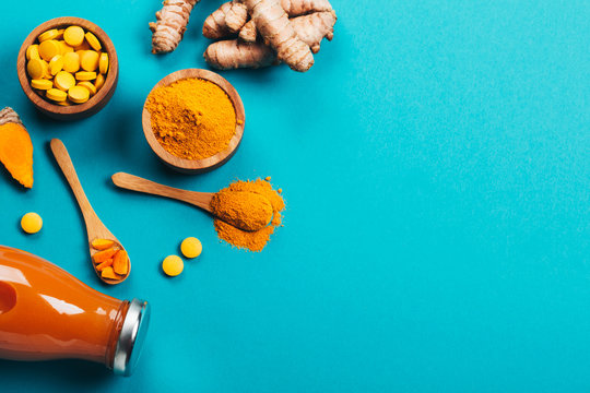 Mess of turmeric plant in different conditions: fresh, dry root, pills, powder and cut plant on blue background. Flat lay style. Place for text.