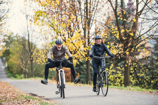 Active senior couple with electrobikes cycling outdoors on a road in nature.