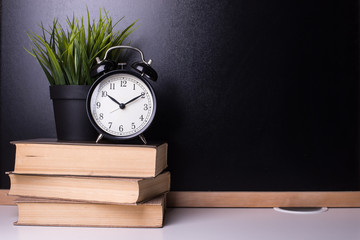 Alarm clock is on books on the background of a blackboard. Learning Concept.