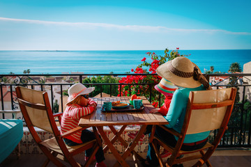 family having breakfast on balcony terrace with sea view