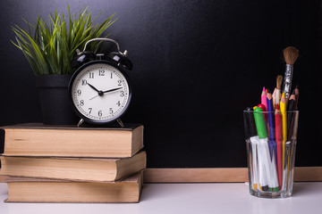 Alarm clock is on books on the background of a blackboard. Learning Concept.