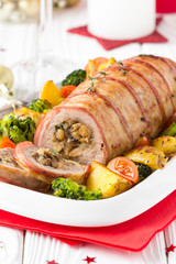 Pork roll wrapped in bacon stuffed with mushrooms and beans, vegetables on the side. Beautiful festive main dish for Christmas holidays