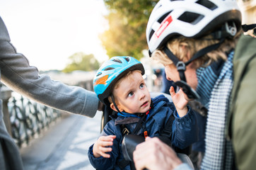 A small toddler boy with helmet and young parents outdoors in city.