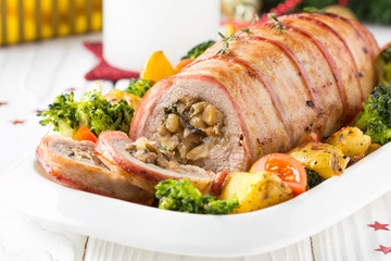 Pork roll wrapped in bacon stuffed with mushrooms and beans, vegetables on the side. Beautiful festive main dish for Christmas holidays