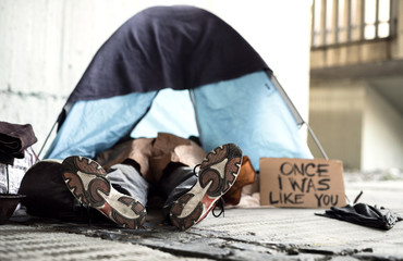 Legs and feet of homeless beggar man lying on the ground in city, sleeping in tent.
