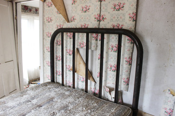 Metal bed frame in abandoned house with peeling wallpaper