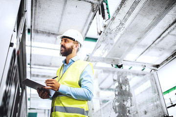A portrait of an industrial man engineer with clipboard in a factory, working.