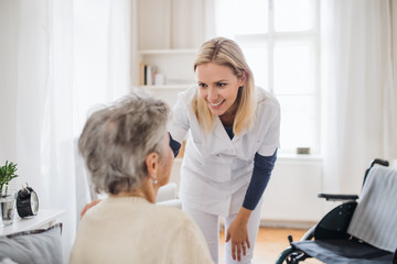 A health visitor talking to a senior woman sitting on bed at home.